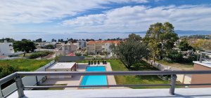 Υπερυψωμένη λήψη πάνω από την πισίνα της βίλας, που δείχνει τον κήπο, τις ξαπλώστρες και τη θάλασσα.