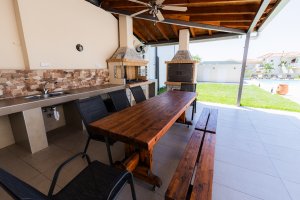 Σκεπασμένος χώρος BBQ στη Villa Memories στην Κινέτα με ξύλινο τραπέζι, καθίσματα και ψησταριές